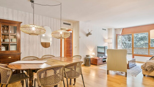 A dining area with a wooden table and wicker chairs, a wooden cabinet with glass doors, and a large mirror.