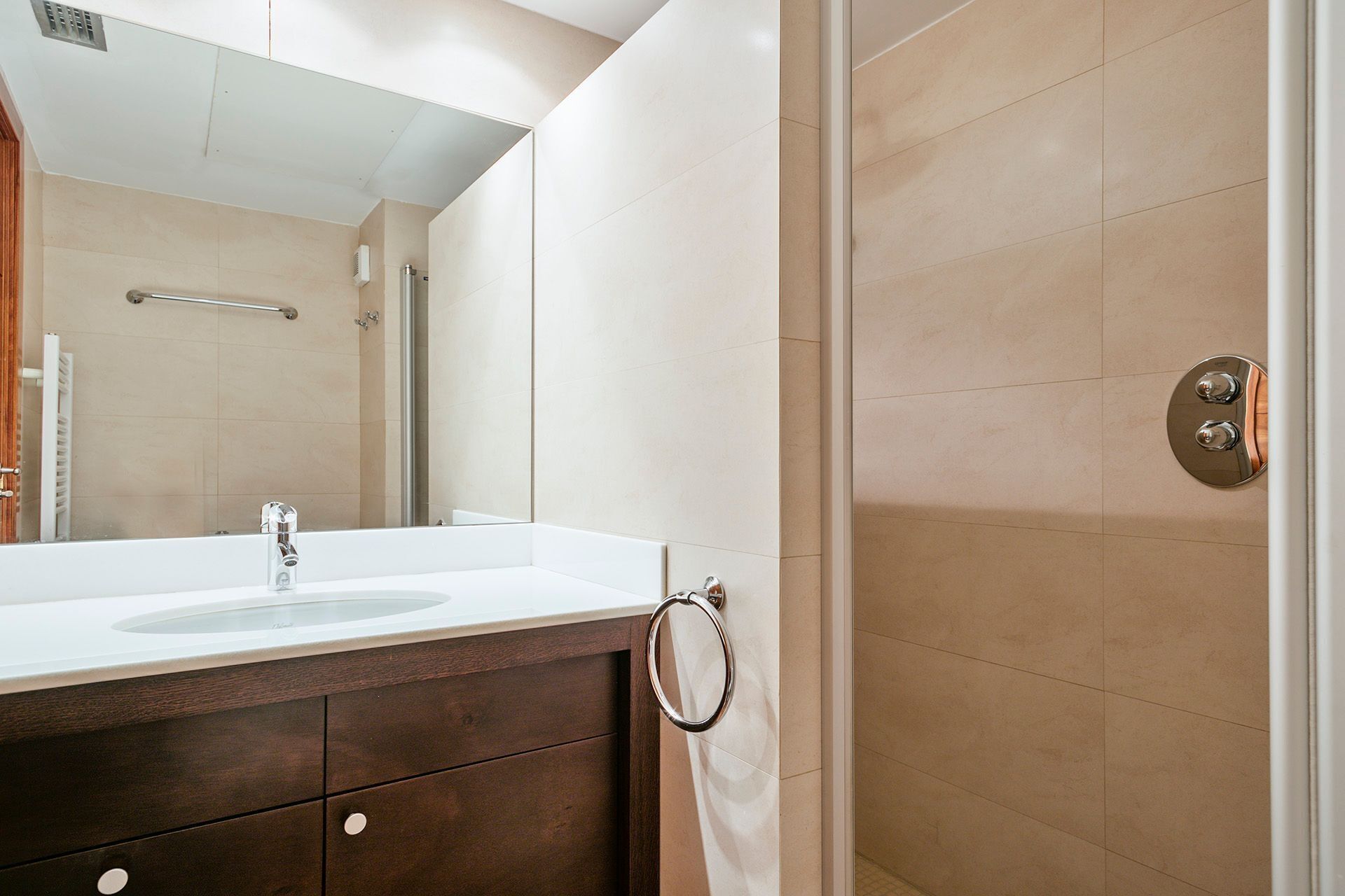 Un baño moderno con un espejo grande, un lavabo, un perchero para toallas y una zona de ducha.