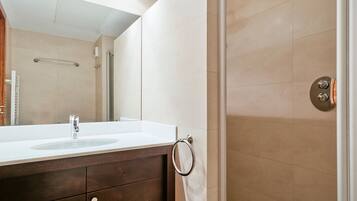 Un baño moderno con un espejo grande, un lavabo, un perchero para toallas y una zona de ducha.