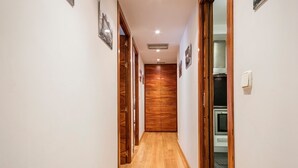 A hallway with wooden flooring, a wooden wardrobe, and a white wall with a light switch.