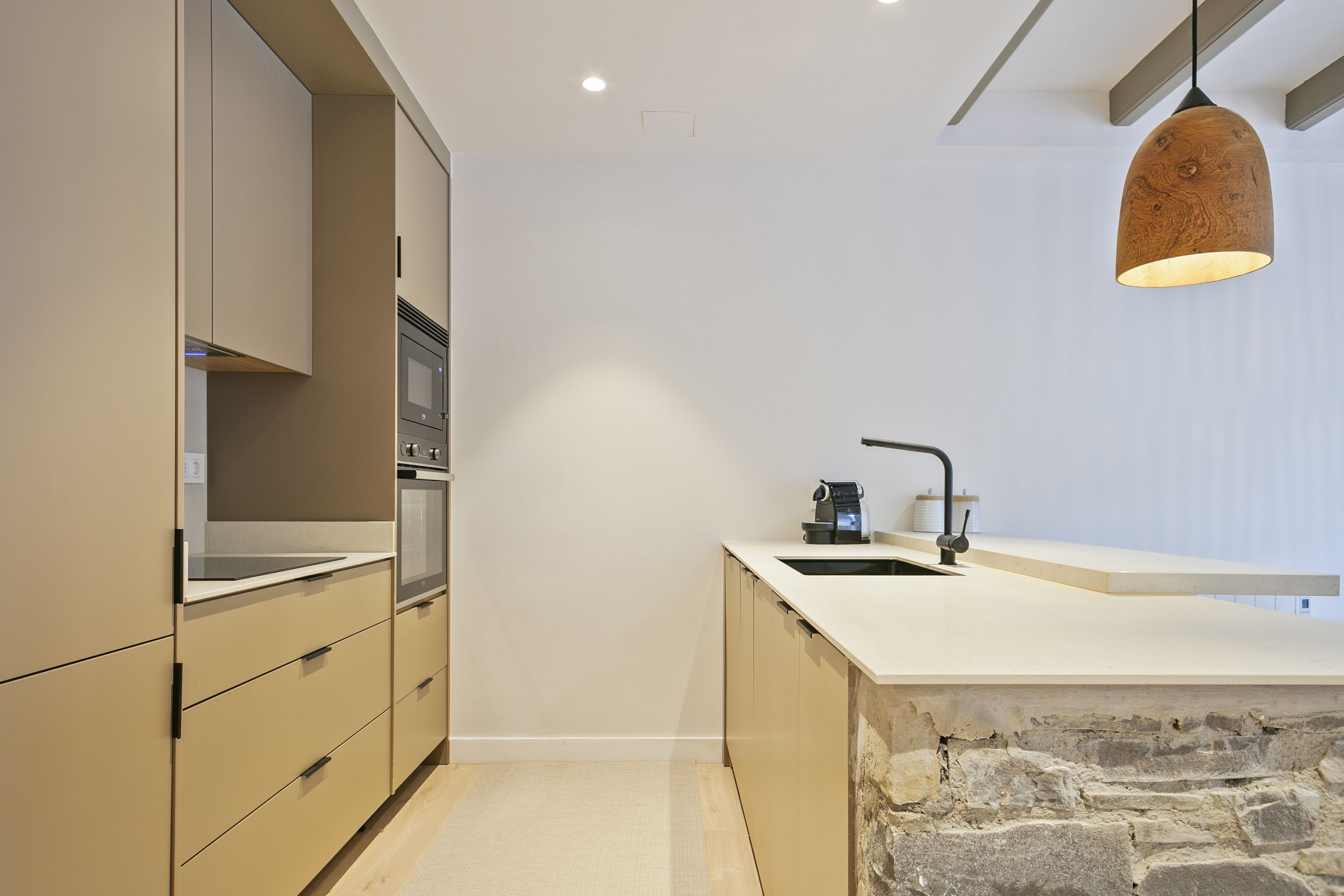 A modern kitchen with a stone accent wall, a built-in oven, and a pendant light.