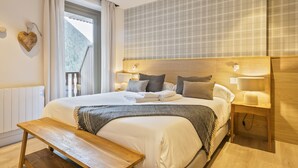 Ein ordentlich eingerichtetes Schlafzimmer mit einem großen Bett, Nachttischlampen, einer Bank und Blick ins Freie.