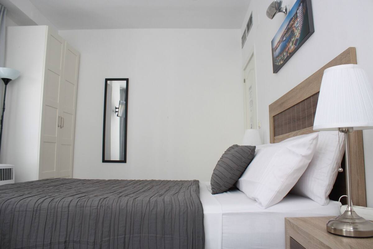 Habitación de hotel con cama, lámpara de noche, mesita de noche y un cuadro en la pared.