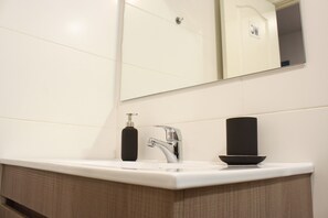 Un baño moderno con un lavabo blanco, un grifo cromado, un dispensador de jabón negro y un jabonera negra.