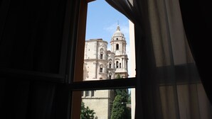 A view of a historic building with a prominent dome and bell tower through a window with curtains. - The Catherdral Rooms (Málaga)