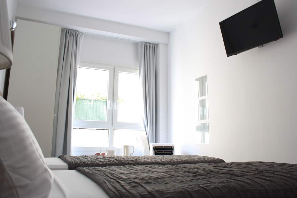 Una habitación de hotel con cama, televisor montado en la pared y ventana con cortinas.