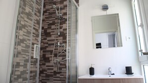 A modern bathroom with a glass-enclosed shower, a vanity with a mirror, and a window providing natural light. - The Catherdral Rooms (Málaga)