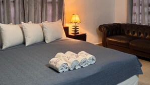 Un lit bien fait, recouvert d’une couette bleue, un canapé en cuir marron et une lampe de chevet.
