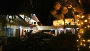 Un immeuble à plusieurs étages doté d’un espace extérieur couvert, qui pourrait être un restaurant ou un salon, et une piscine en arrière-plan.