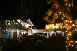 Un edificio de varios pisos con un espacio al aire libre cubierto, posiblemente un restaurante o un salón, y una zona de piscina al fondo.