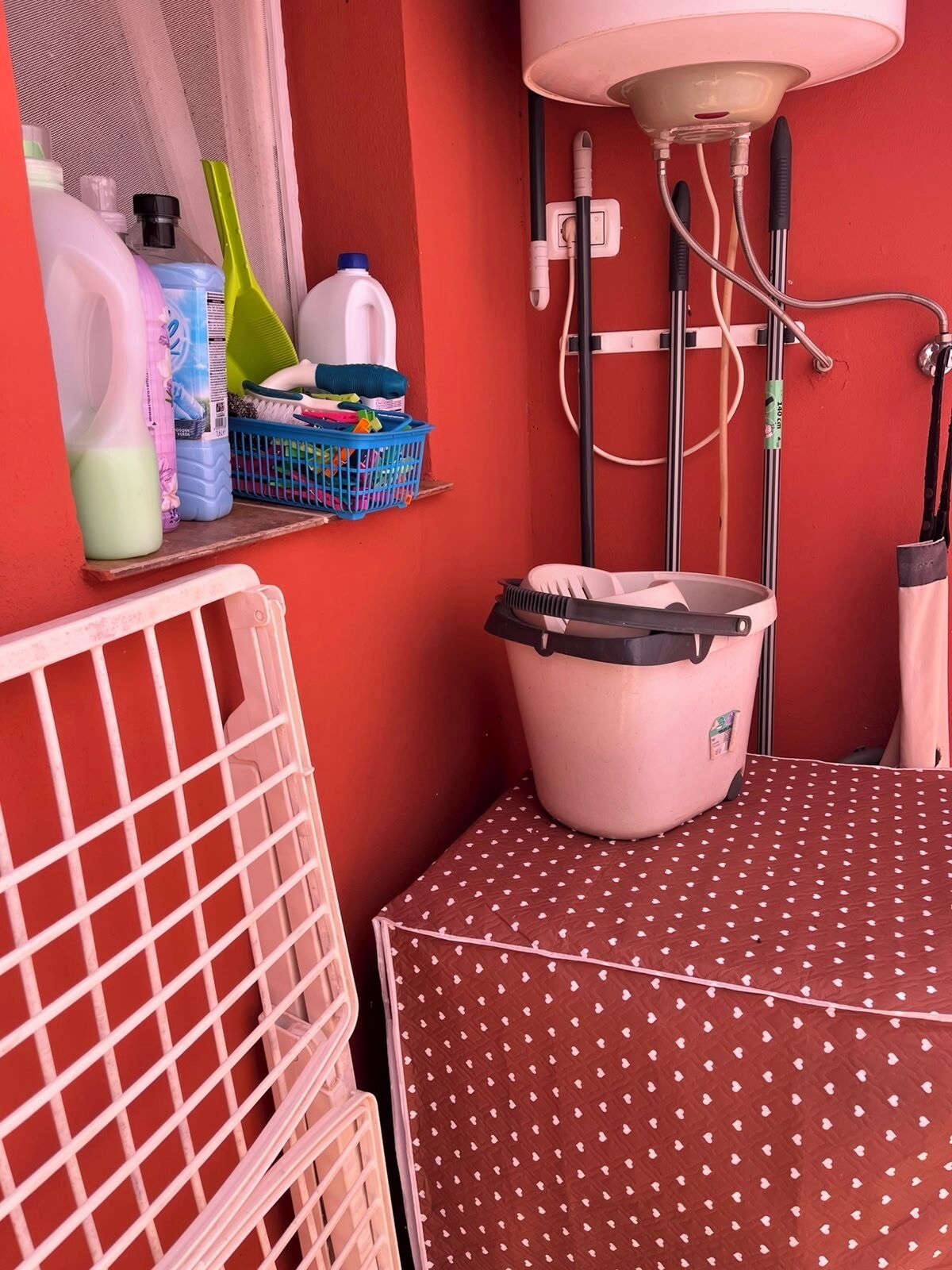 Ein Badezimmer mit roter Wand, einem weißen Waschbecken, einer pinkfarbenen Mülltonne und einem Regal mit Reinigungsmitteln.