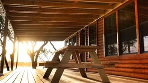 A wooden deck with a picnic table, large windows, and a view of trees.