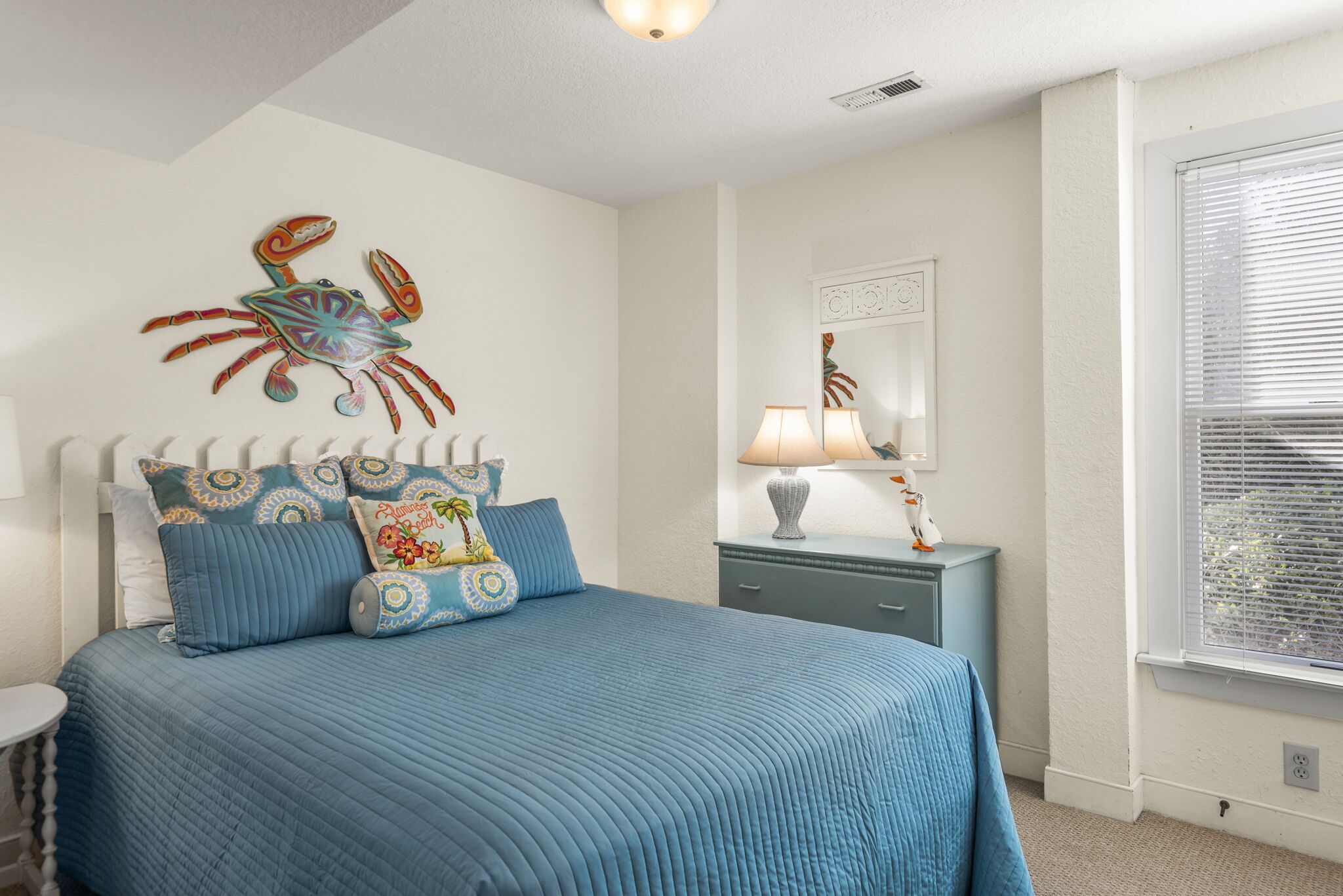 A bedroom with a bed, a nightstand, a lamp, a mirror, and a window.