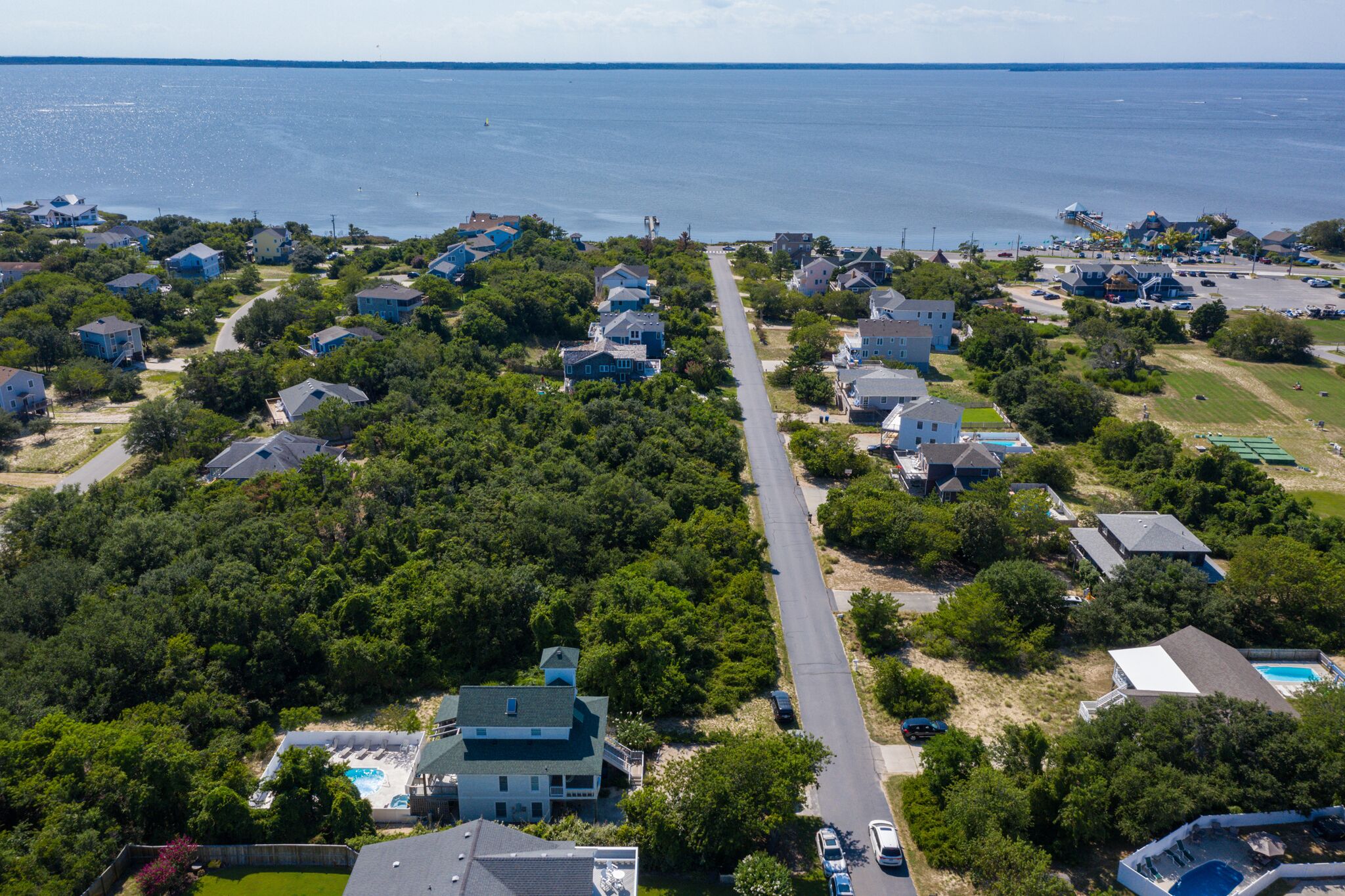 An aerial view of a coastal residential area with houses, a road, and a beach.