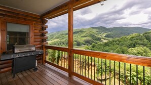 A wooden deck with a grill and a view of a mountainous landscape.