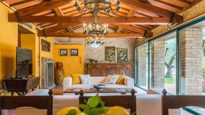 A cozy living room with a wooden ceiling, a fireplace, a dining table, and a large window. - Villa Cavalli - Private villa, 4 bedrooms, pool, A/C, wifi, nature, Marche (Vallefoglia)