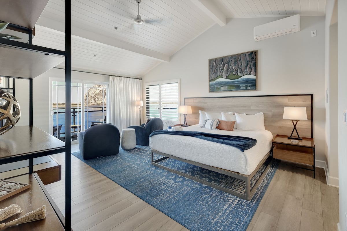 A modern hotel room with a large bed, a desk, a chair, and a view of the sea.