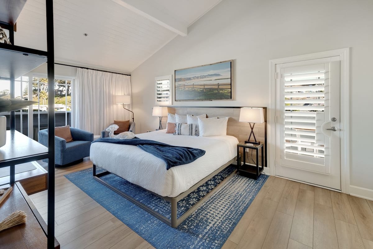 A bedroom with a large bed, a desk, a chair, and a view of the outdoors.