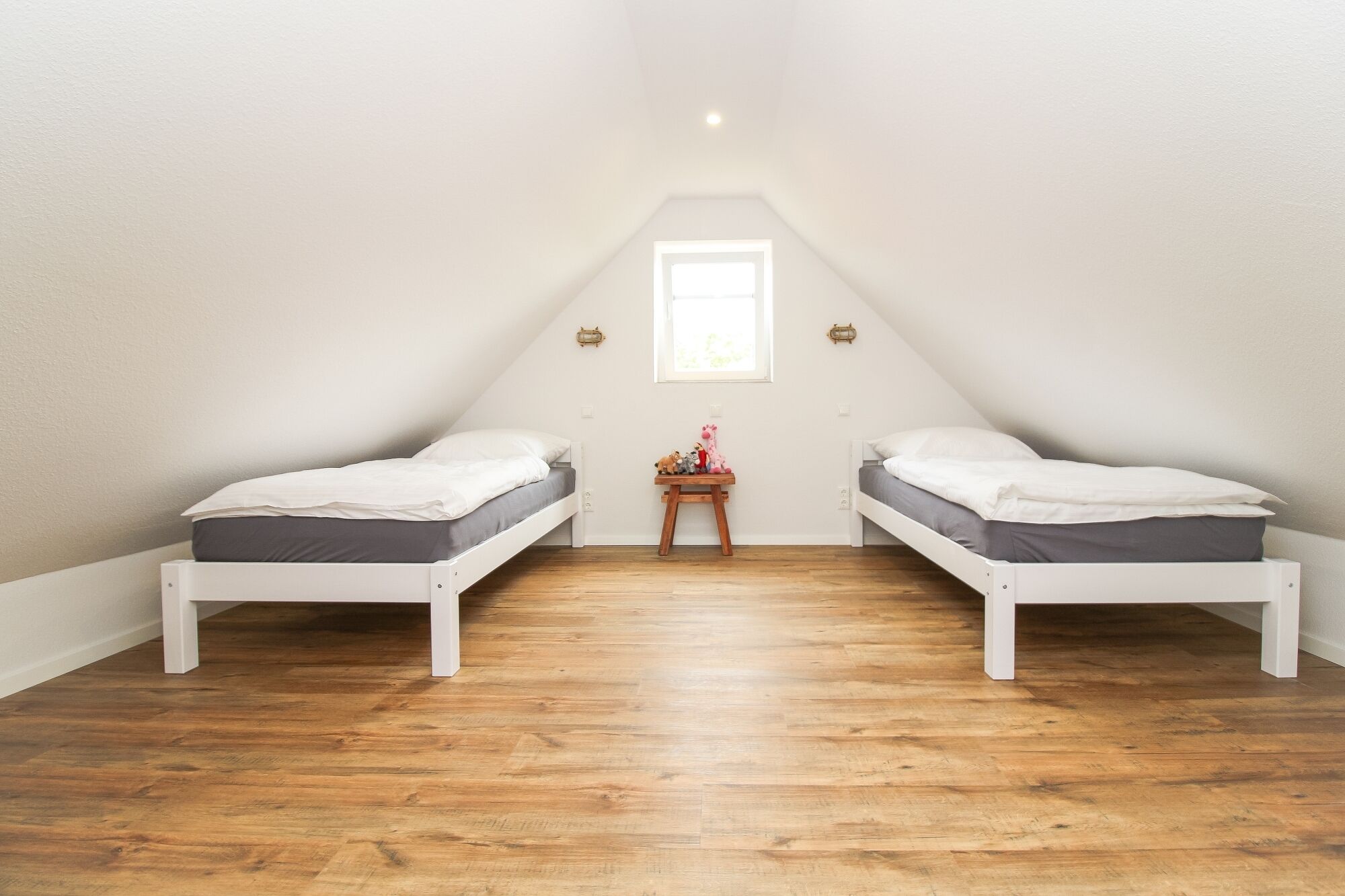 A small, triangular attic bedroom with two white beds, a wooden floor, and a small table with toys.