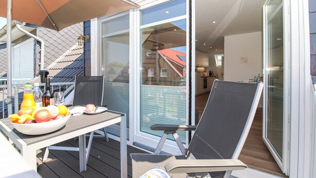 Een balkon met een tafel gedekt voor een maaltijd, een stoel en een waterfles.