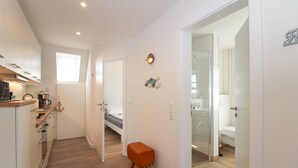 Een compacte hotelkamer met kitchenette, een kleine badkamer met douche en een bed in de hoek.