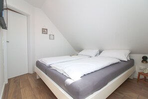 A small, single-bed room with a sloped ceiling, a wooden floor, and a bedside table with a lamp.
