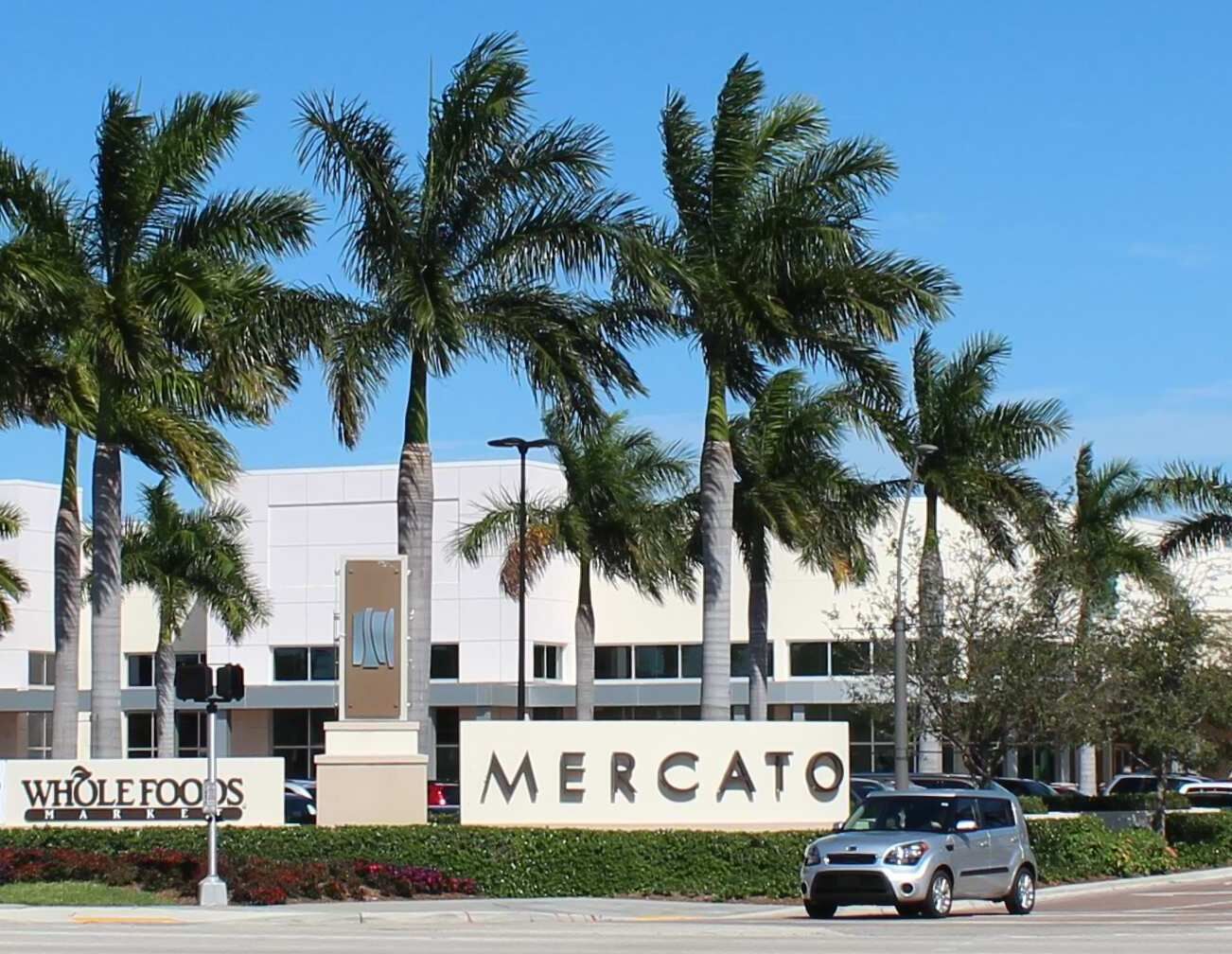 Un bâtiment du magasin Whole Foods Market, avec une enseigne indiquant « MERCATO » et des palmiers au premier plan.