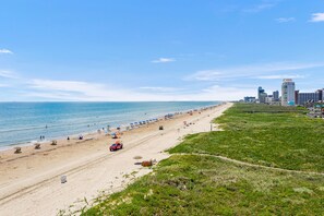 A beach with a sandy shore, umbrellas, and a few people. There are buildings in the background. - Beachfront SPI Getaway! (South Padre Island)