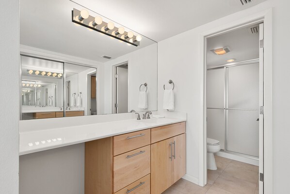 A modern bathroom with a large mirror, vanity, and a shower enclosure. - Beachfront SPI Getaway! (South Padre Island)