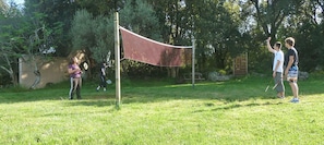 Ein grünes Freigelände mit Volleyballnetz, Bäumen und einem Holzzaun.