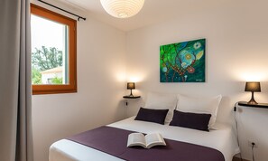 A bedroom with a bed, two bedside lamps, a painting on the wall, and a window with curtains. - 2-bedroom apartment on an 8-hectare estate, on the shores of Lake Teppe Rosse, 7 km from the beaches, air conditioning, Wi-Fi (Aléria)