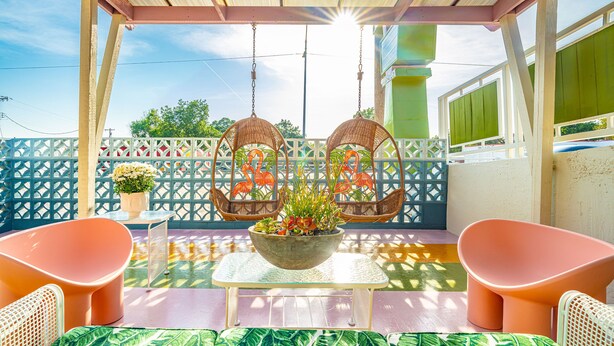 Un espace extérieur abrité, aménagé avec des chaises en osier, une table ornée d’un vase de fleurs et offrant une vue sur un bâtiment en arrière-plan.