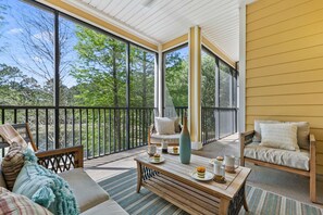A sunlit balcony with a sofa, a table with a vase, and a view of trees. - Upgraded  Luxury Apartment With Communal Pool only 10 Minutes to Disney. (Kissimmee)