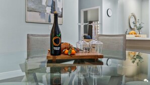 Une table en verre avec une bouteille, des verres et des oranges.