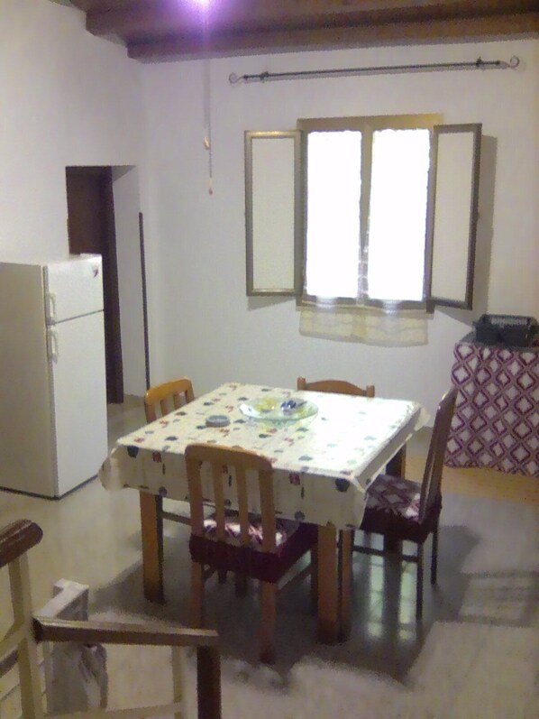 A small dining area with a table, chairs, a refrigerator, and a window with curtains.