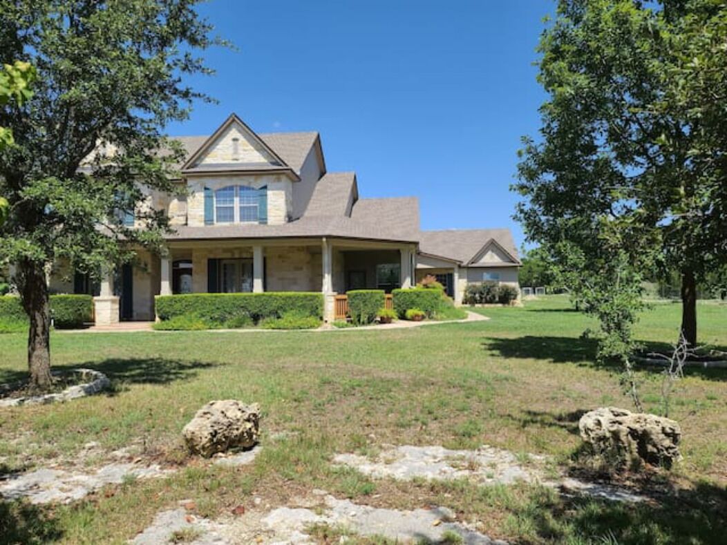 Une maison à deux étages avec une façade en pierre, un porche couvert et une pelouse bien entretenue agrémentée de gros rochers.