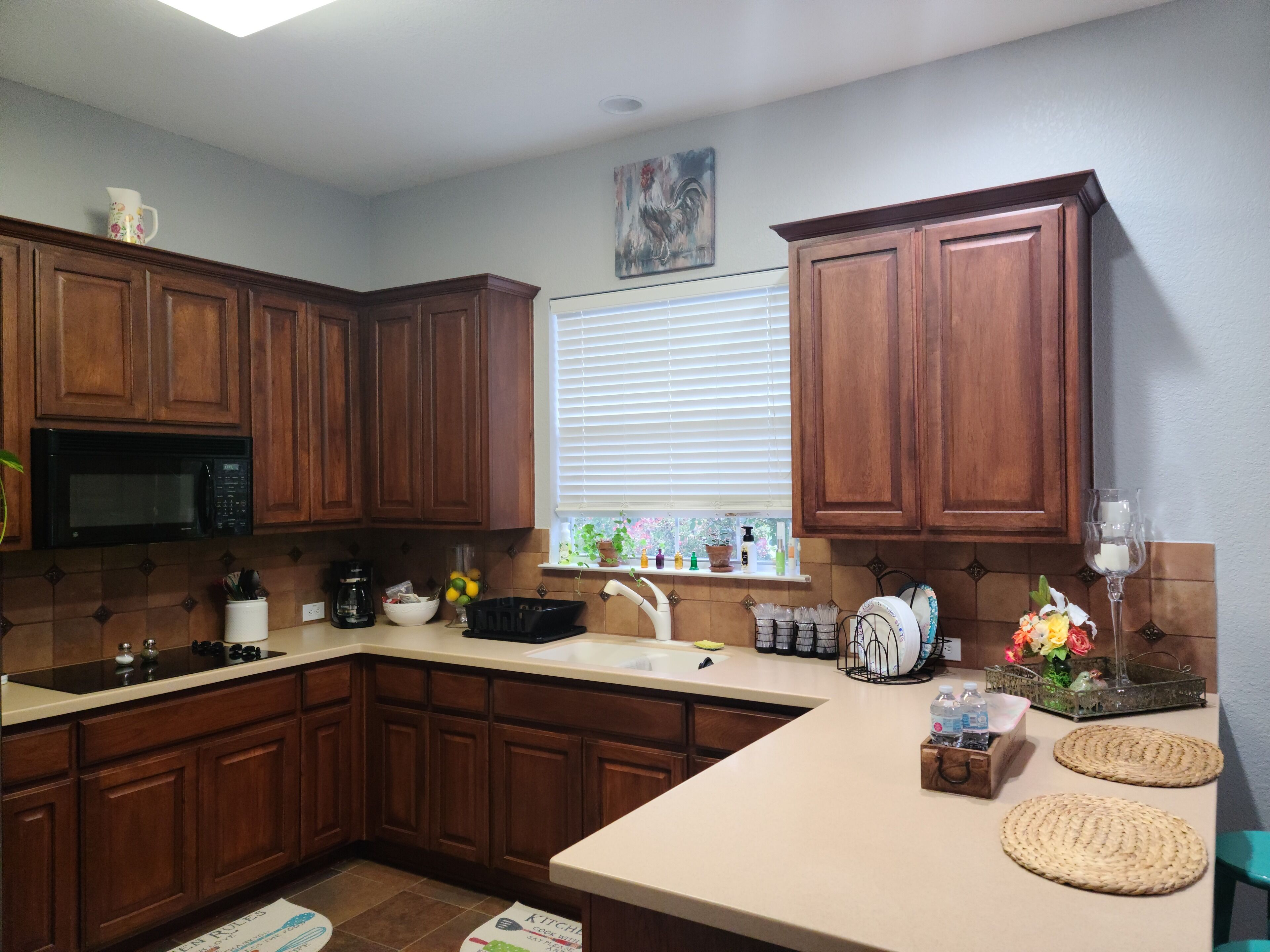 A kitchen with wooden cabinets, a microwave, a sink, and various kitchen items on the counter.