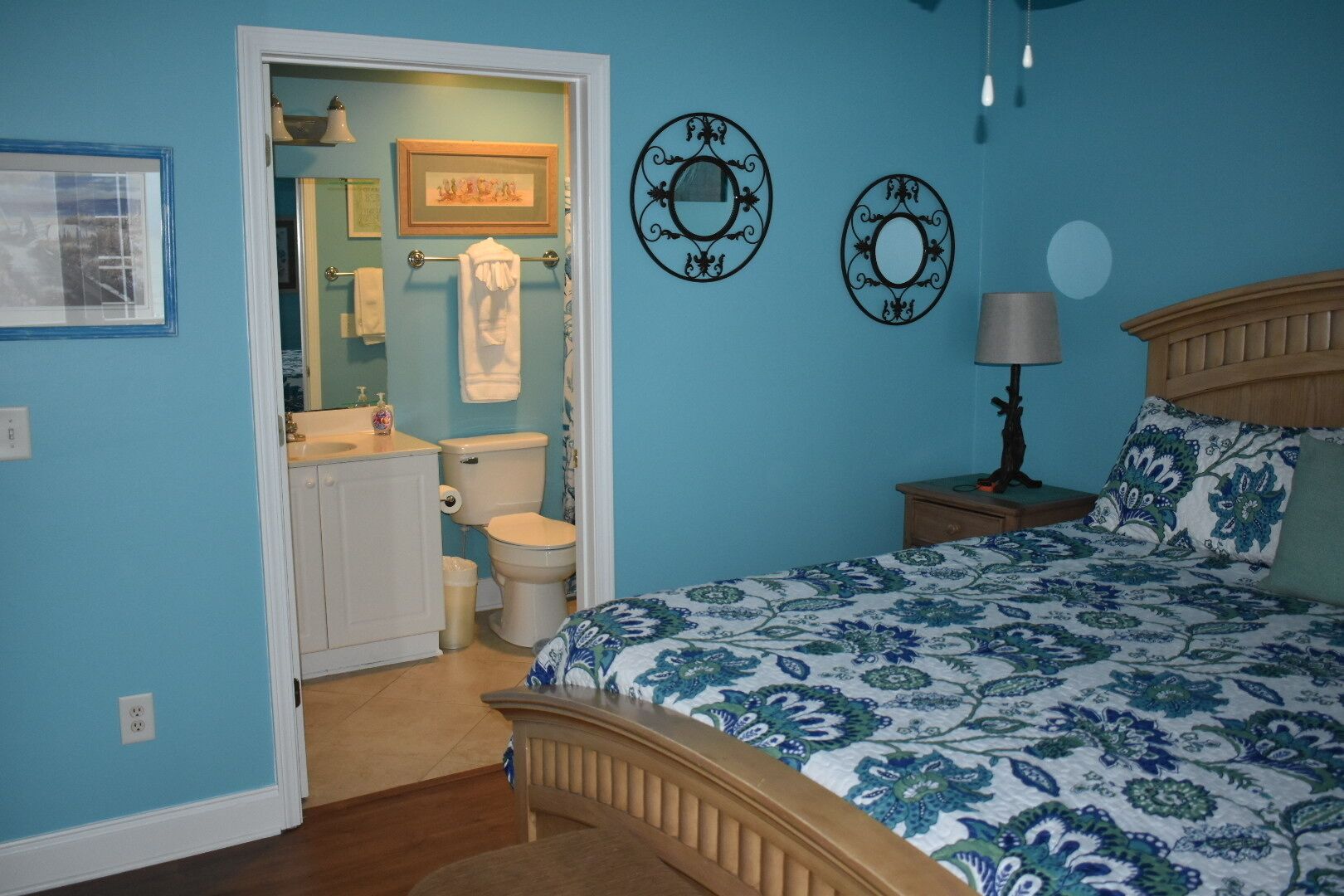 A bedroom with a bed, a nightstand, a lamp, and a wall with two decorative mirrors.