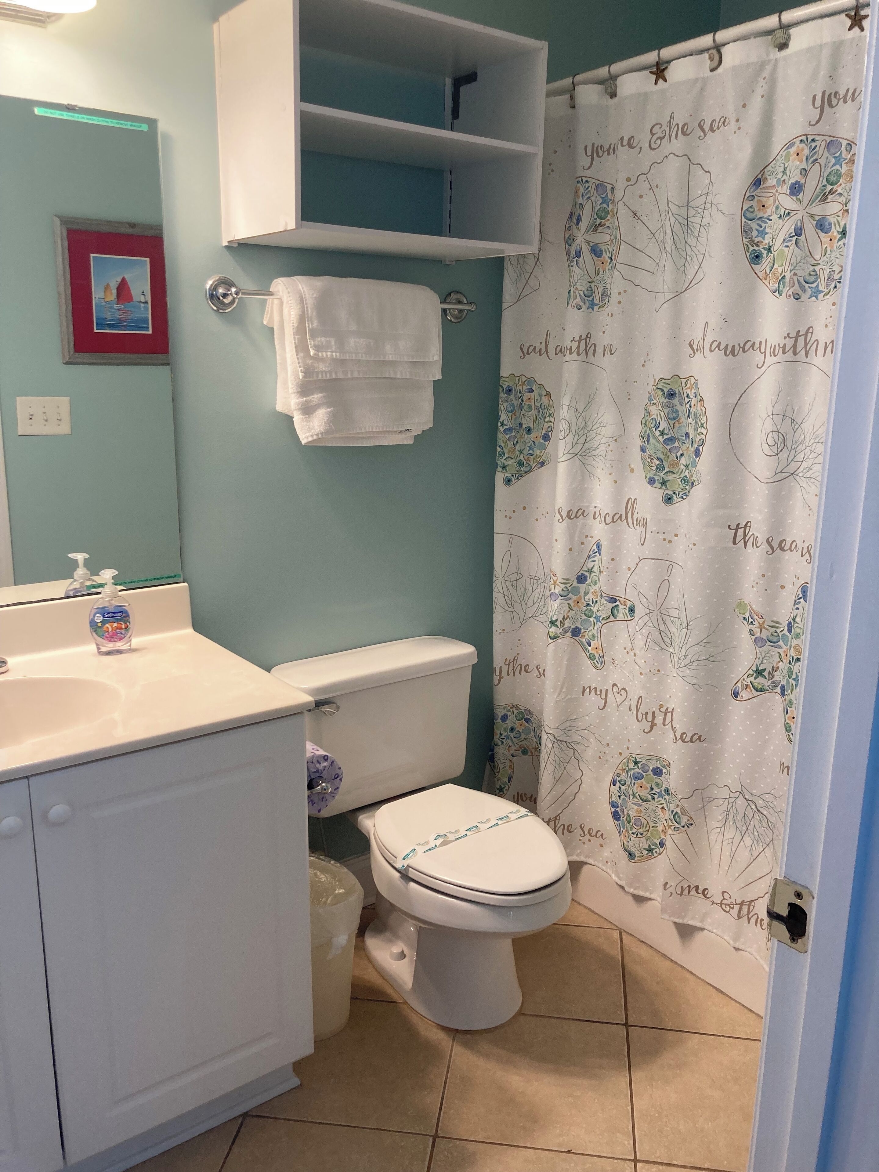 A bathroom with a toilet, sink, and a shower curtain with nautical designs.