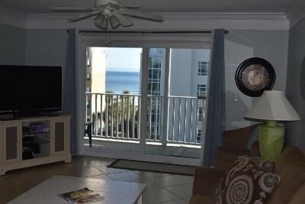 A living room with a television, a coffee table, a lamp, and a balcony with a view of the ocean.