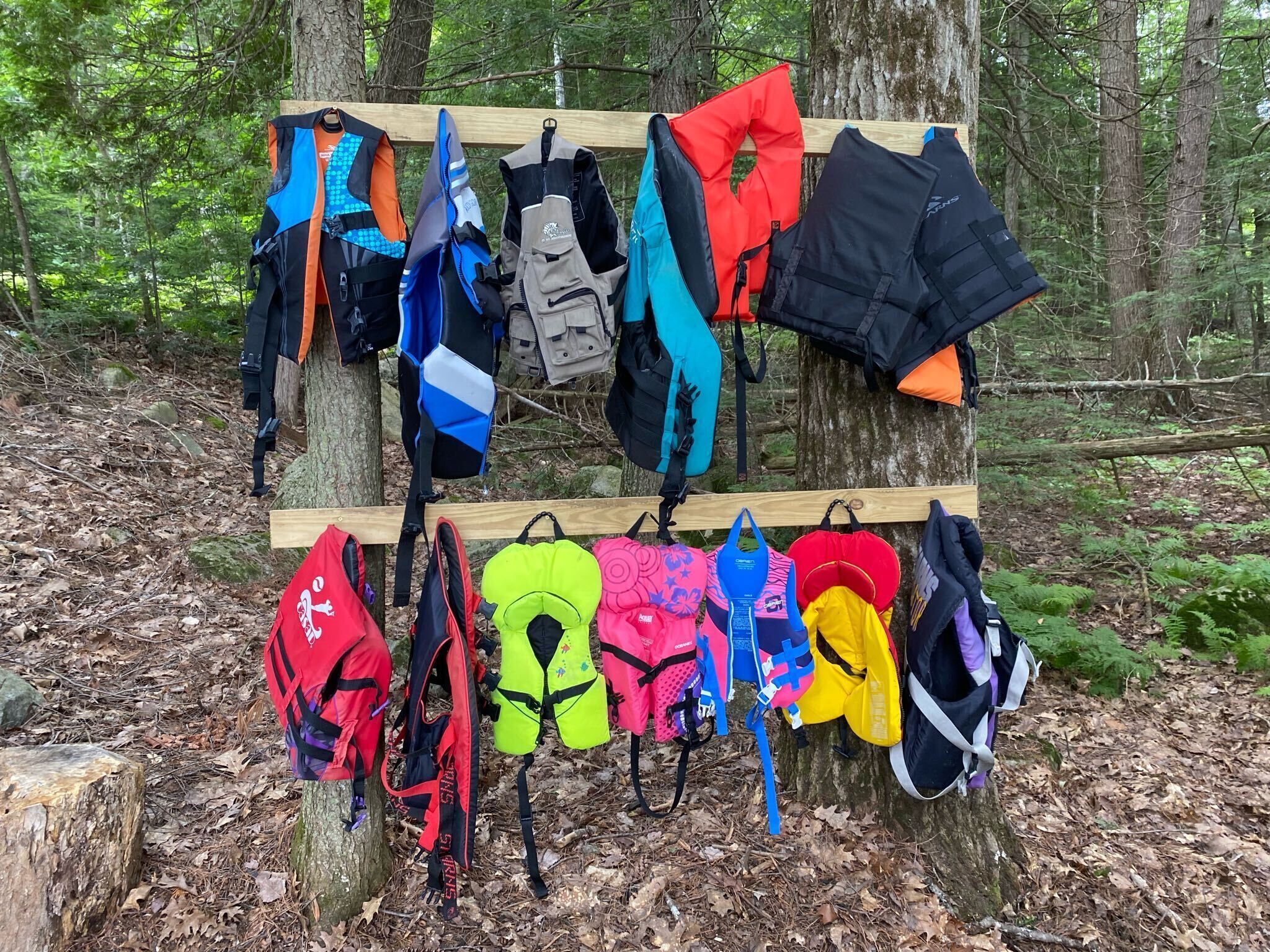A variety of backpacks and jackets hanging on a wooden rack in a forested area.