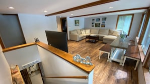 Uma sala de estar espaçosa com escada de madeira, televisão de tela plana, um conjunto de sofás e uma mesa de jantar.