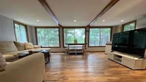 Uma sala de estar espaçosa com um sofá grande, uma mesa de centro, um piano e uma TV sobre um móvel branco.