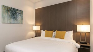 A hotel room with a large bed, two bedside lamps, and a painting on the wall. - Suite 1 with Kitchenette (St. John)