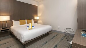 A hotel room with a large bed, two bedside lamps, a desk with a chair, and a wardrobe. - Suite 1 with Kitchenette (St. John)