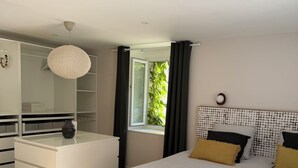 A bedroom with a bed, a dresser, a wardrobe, a window with curtains, and a hanging light fixture.
