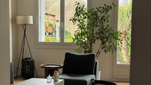 A living room with a sofa, a coffee table, a floor lamp, a potted plant, and a view of the outside.