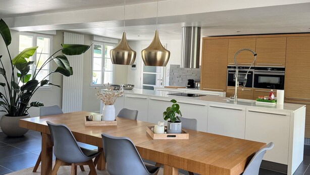 A modern kitchen with a central island, pendant lights, and a dining area with a wooden table and chairs.