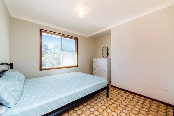 Une chambre à coucher comprenant un lit, une commode, une fenêtre avec des stores et un sol à motifs hexagonaux.