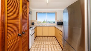 Een praktische keuken met een kookplaat, spoelbak en koelkast, met een groot raam en een houten deur.